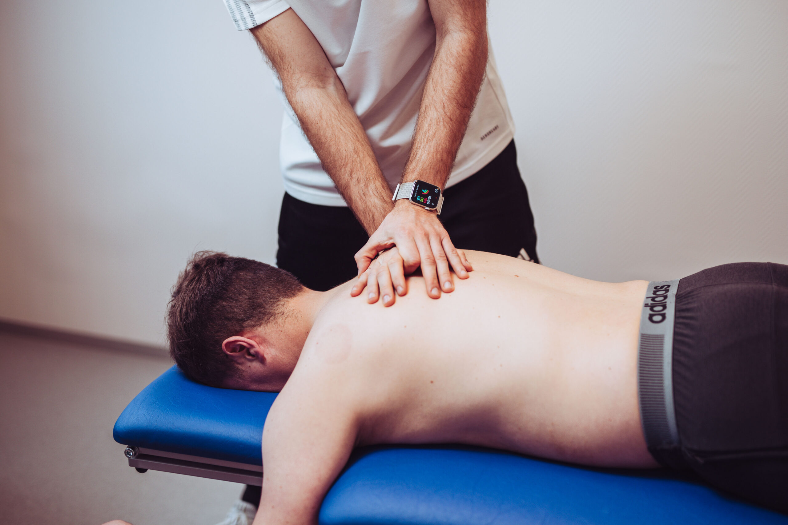 Der Therapeut behandelt den Rücken des Patienten. Dabei handelt es sich um eine physiotherapeutische Behandlung.